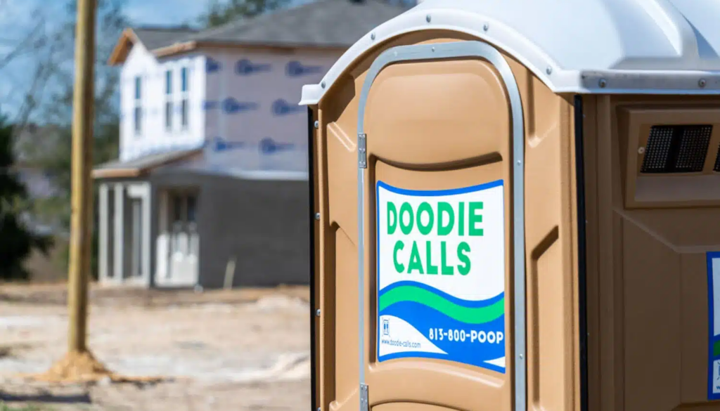 Tan Doodie Calls standard porta potty rental unit on a construction site