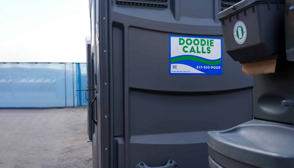 Gray portable toilet and handwashing station at a construction site with a blue fence