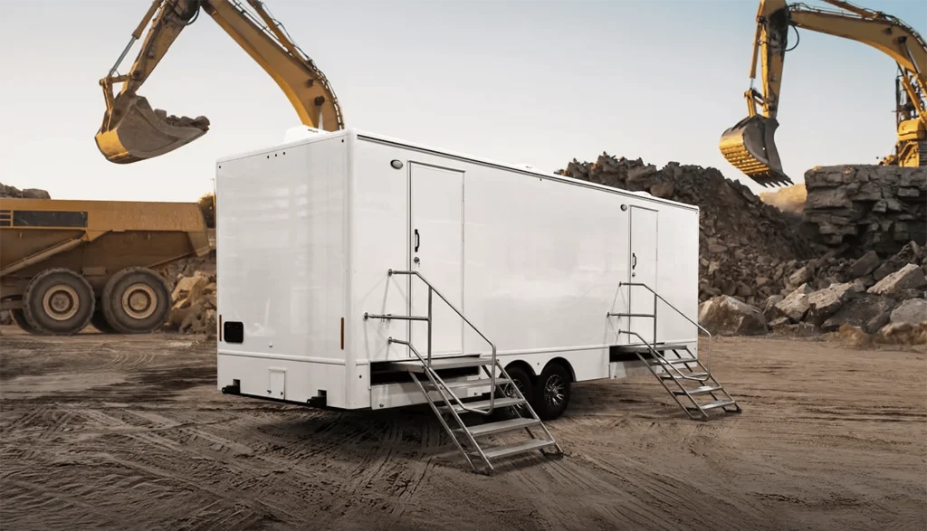 Shower trailer at a construction site with dirt ground and heavy machinery