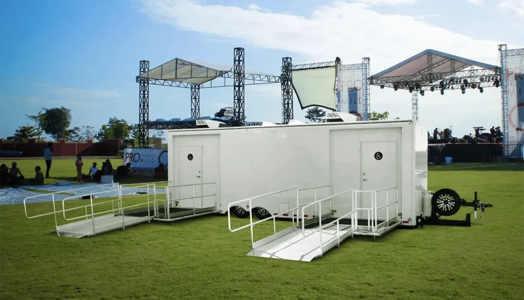 ADA Shower Trailer sitting on the lawn at an outdoor music festival with a stage behind it